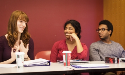 Photograph of a red haired student speaking in class as two of her peers look on attentively