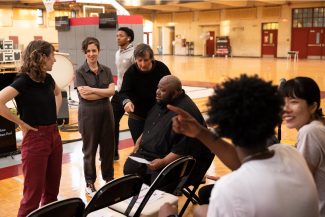 Director Brooke O'Harra converses with composer Tyshawn Sorey in the Girard College gym. Five other collaborators listen in, including musicians Julian Den Boer and Laura Barger.