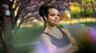 A photograph of Kelly Garcia-Ramos taken on the Penn campus. They are crossing their arms and looking into the distance with an expression of confidence and optimism.