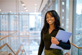 A professional photograph of Gwen Lewis smiling and holding a folder in the offices of the New York Times.