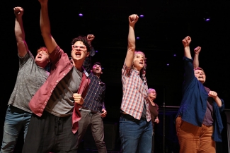 A photograph of a group of actors raising their fists in the air